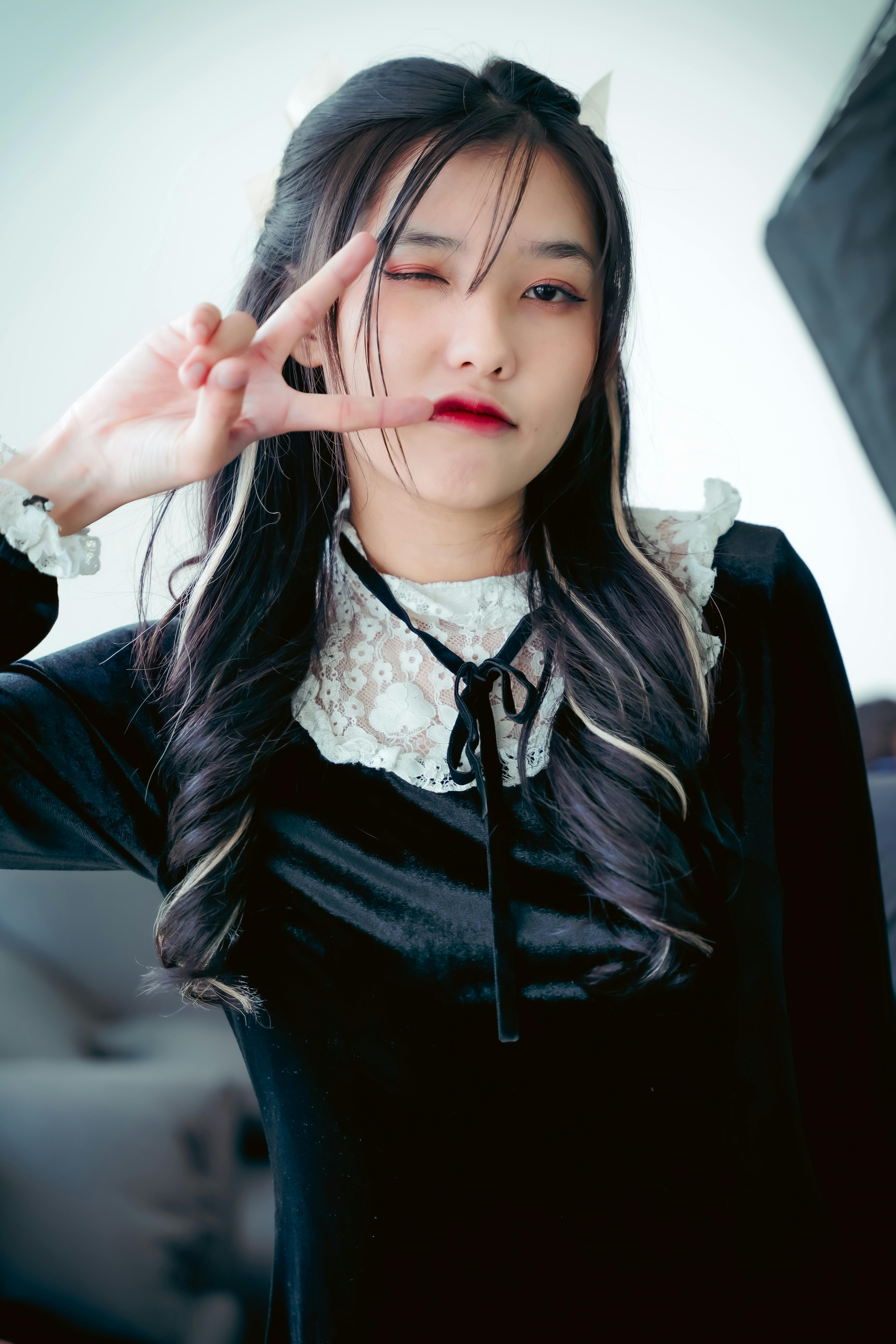 Young woman in a black velvet dress poses with peace gesture indoors. Fashion portrait.