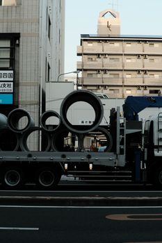 Truck carrying large pipes on a city street during the day, captured in an urban environment.