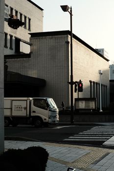 A truck waits at a traffic light on a quiet urban street corner in the morning light.