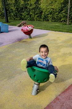Two kids having fun on spinning seats at a colorful outdoor playground.