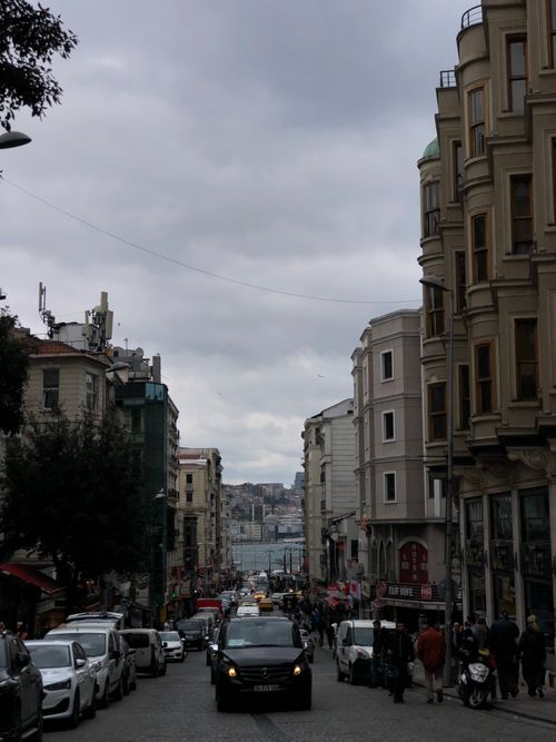 Free Vibrant urban street with historical buildings and bustling traffic under a cloudy sky. Stock Photo