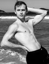 Striking black and white portrait of a shirtless man on a Brazilian beach, showcasing strength and elegance.