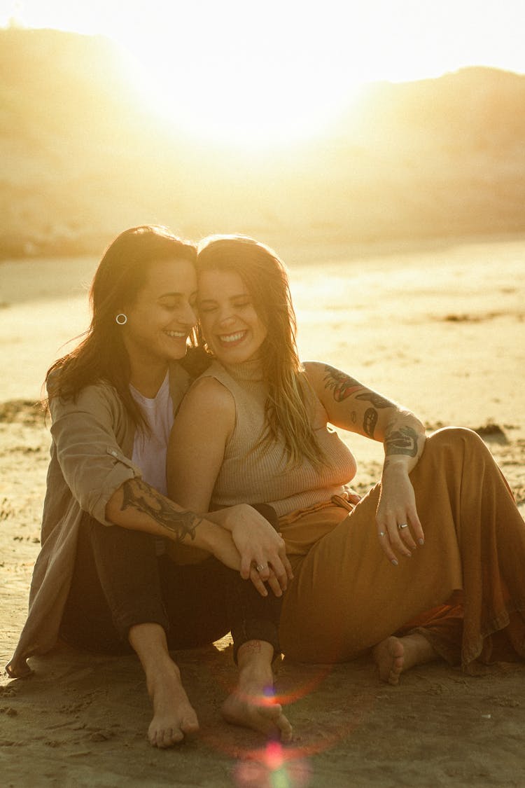 Smiling Couple Sitting On Beach At Sunset