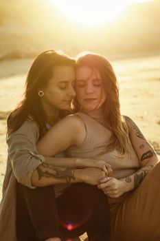 Two women lovingly embracing on a sunny beach during sunset, expressing warmth and affection.