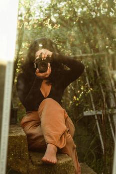 A woman sits on steps, capturing her reflection through a camera in an outdoor setting.