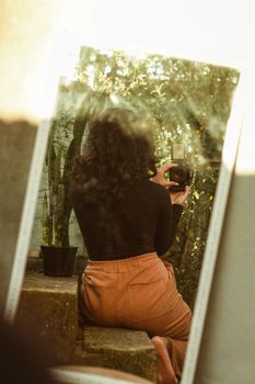 A woman takes a photo of her reflection in a mirror amidst a natural outdoor setting.