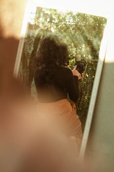 Back view of a woman holding a camera, captured in an outdoor mirror reflection, medium shot.