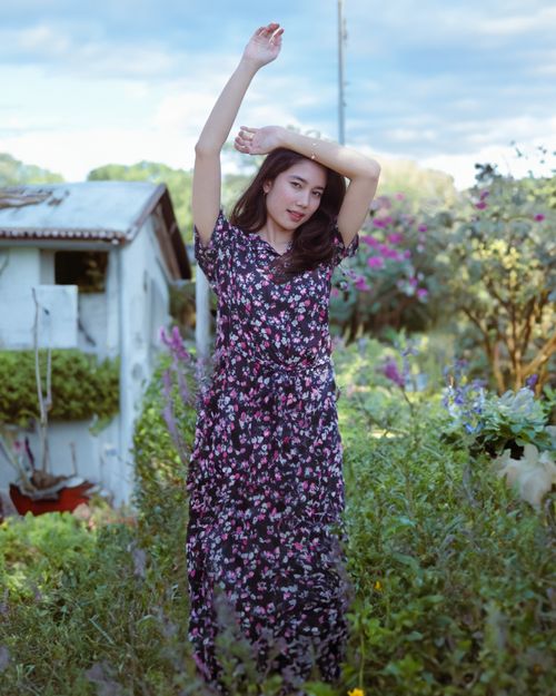 Free A woman in a floral dress posing elegantly in a vibrant garden setting during the day. Stock Photo