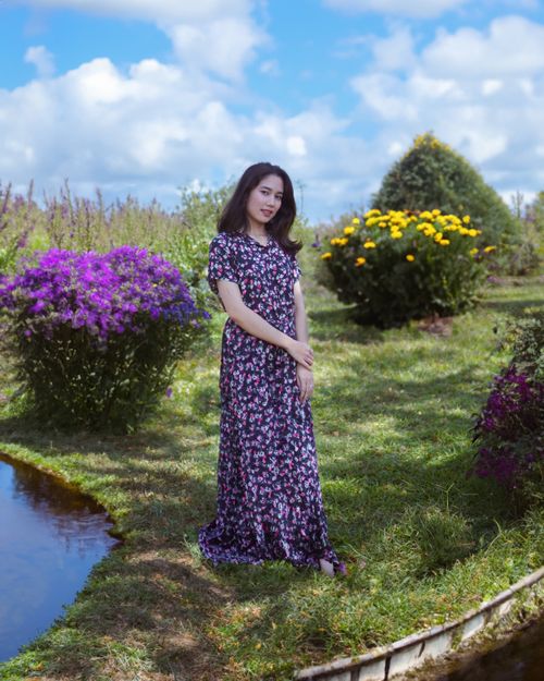 Free A woman in a floral dress standing elegantly in a colorful garden setting. Stock Photo