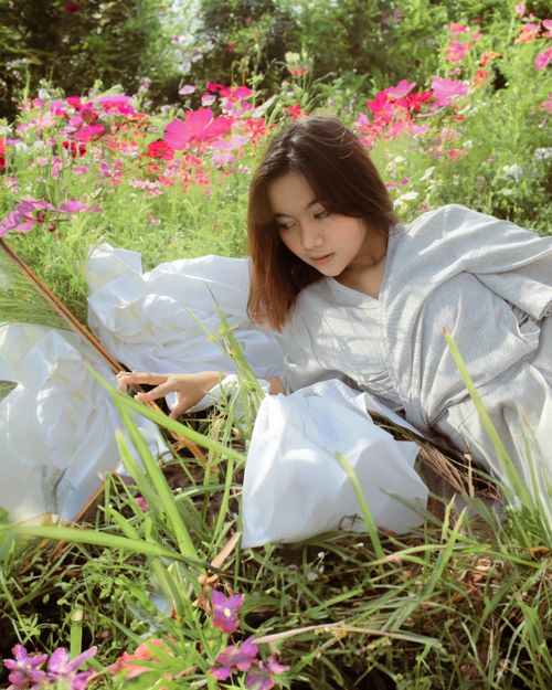 Free Woman wearing a white dress lying in a colorful floral meadow under daylight, exuding tranquility. Stock Photo