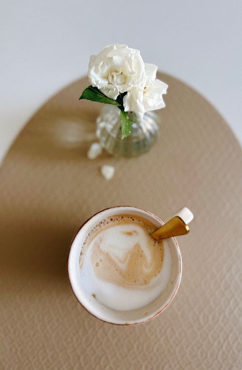 Free A minimalist still life with a cup of coffee and white carnation in a vase on a beige surface. Stock Photo