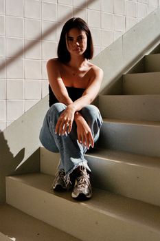 Artistic portrait of a woman sitting on stairs, showcasing natural light and shadows.
