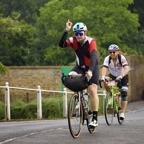 Two cyclists are riding down a road with one waving