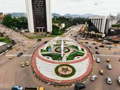 A vibrant aerial view of the 'Love My Country Cameroon' monument in Yaoundé, showcasing urban traffic and cityscape.