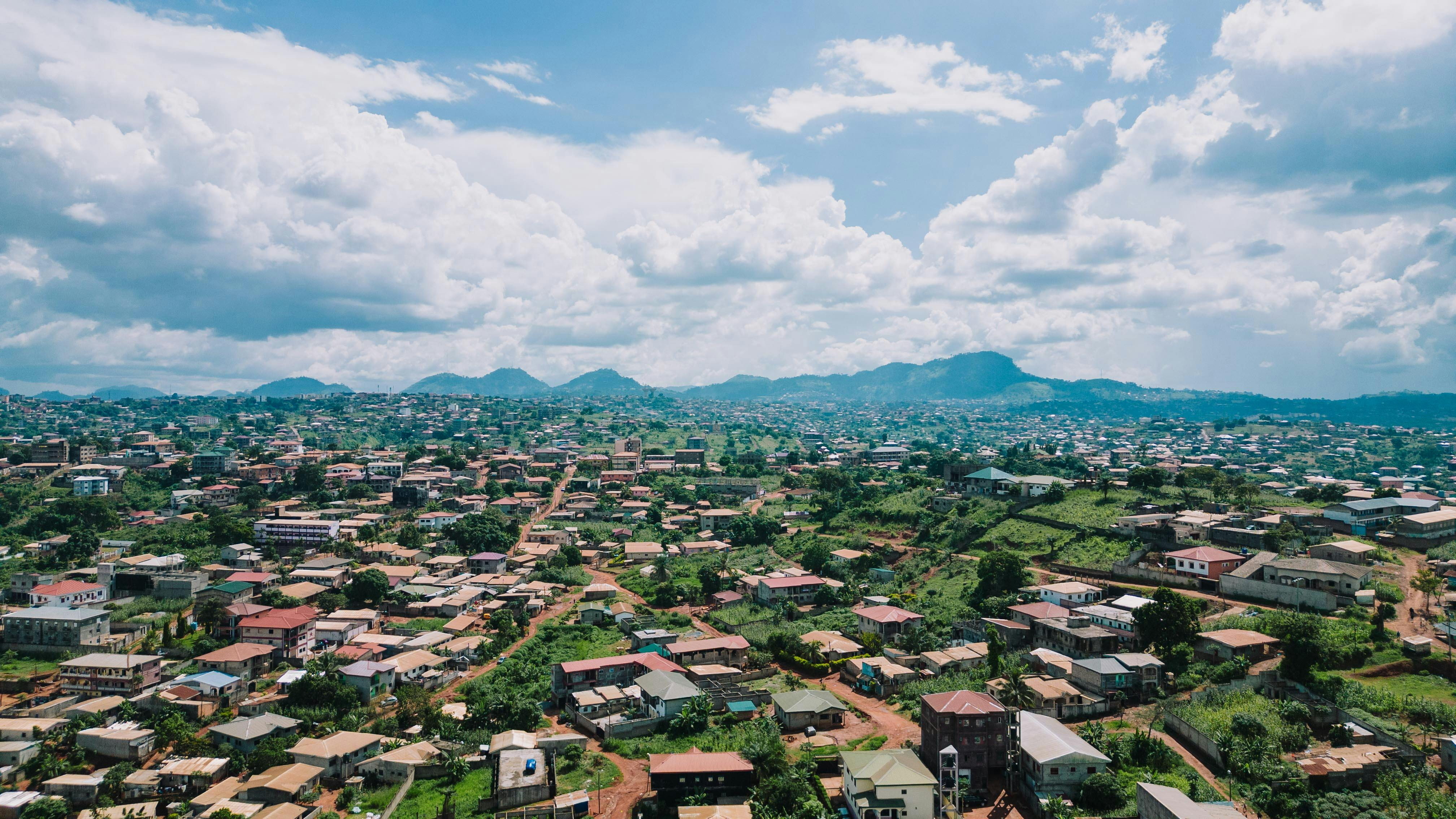 Drone shot of Yaoundé, Cameroon, showcasing a sprawling cityscape against a mountainous horizon under a vibrant sky.