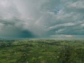 Explore the lush Cameroon rainforest from above, capturing a rainbow amidst dramatic clouds.