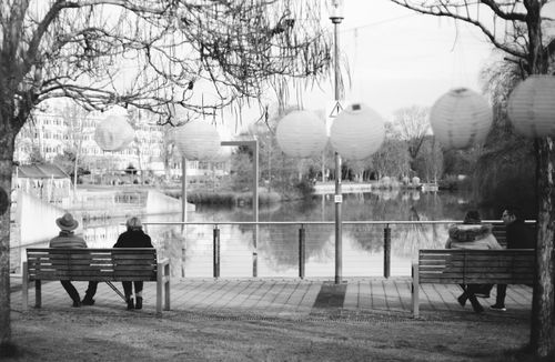 Free Calm scene of people sitting on park benches overlooking a tranquil lake in an urban setting. Stock Photo