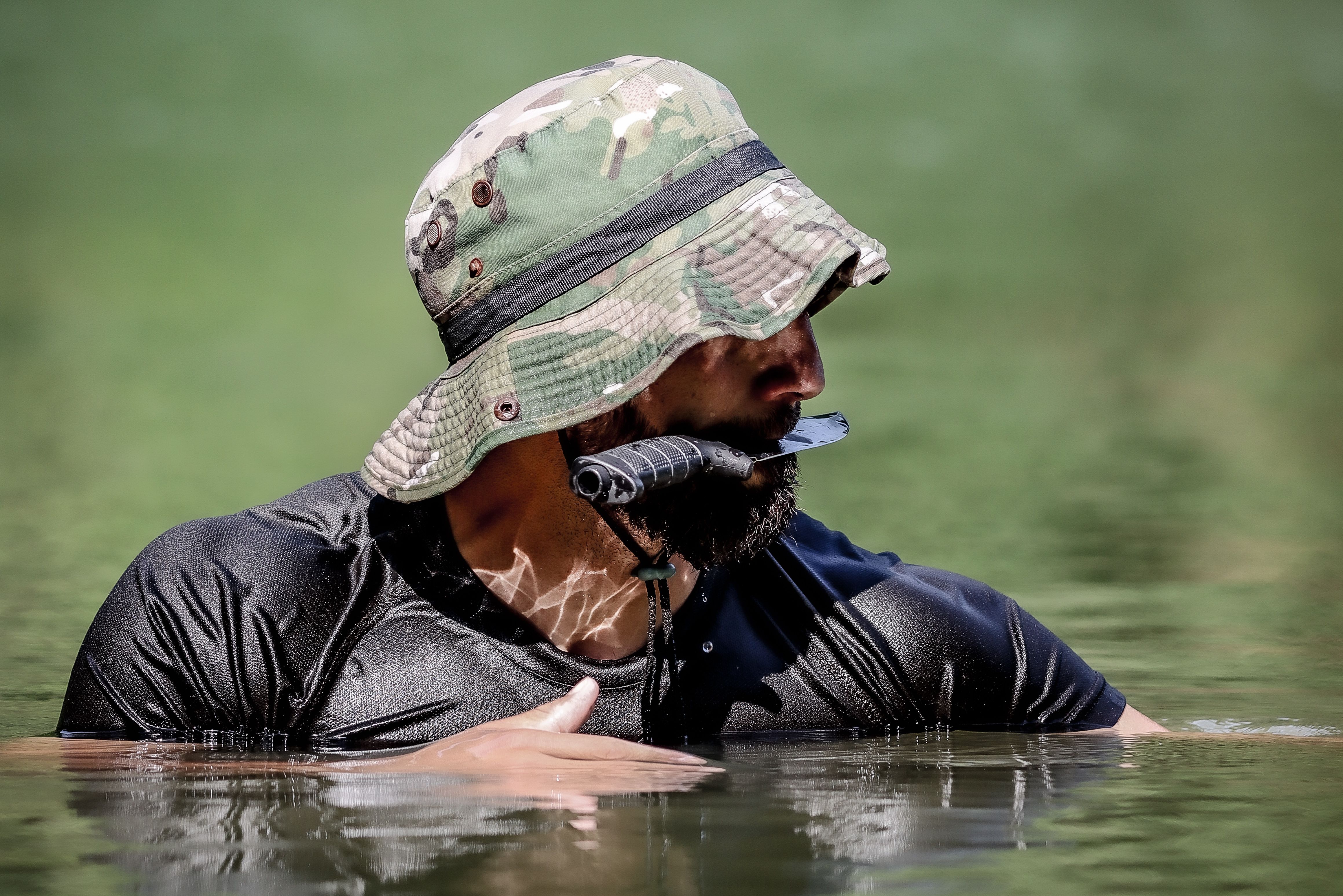 A man in a camo hat holding a knife in the water, showcasing survival skills.