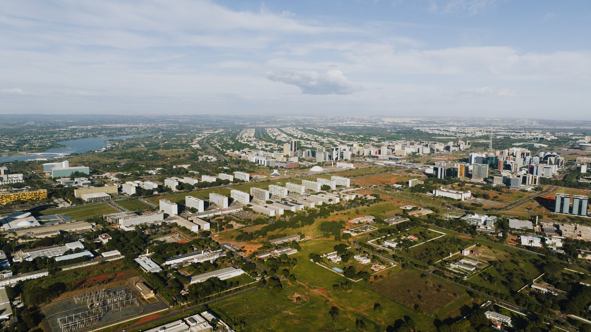 Aerial shot of Brasília showcasing its urban landscape, buildings, and greenery in daylight.