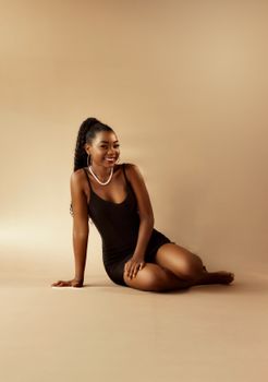 Stylish African American woman in black dress smiling in a studio setting.