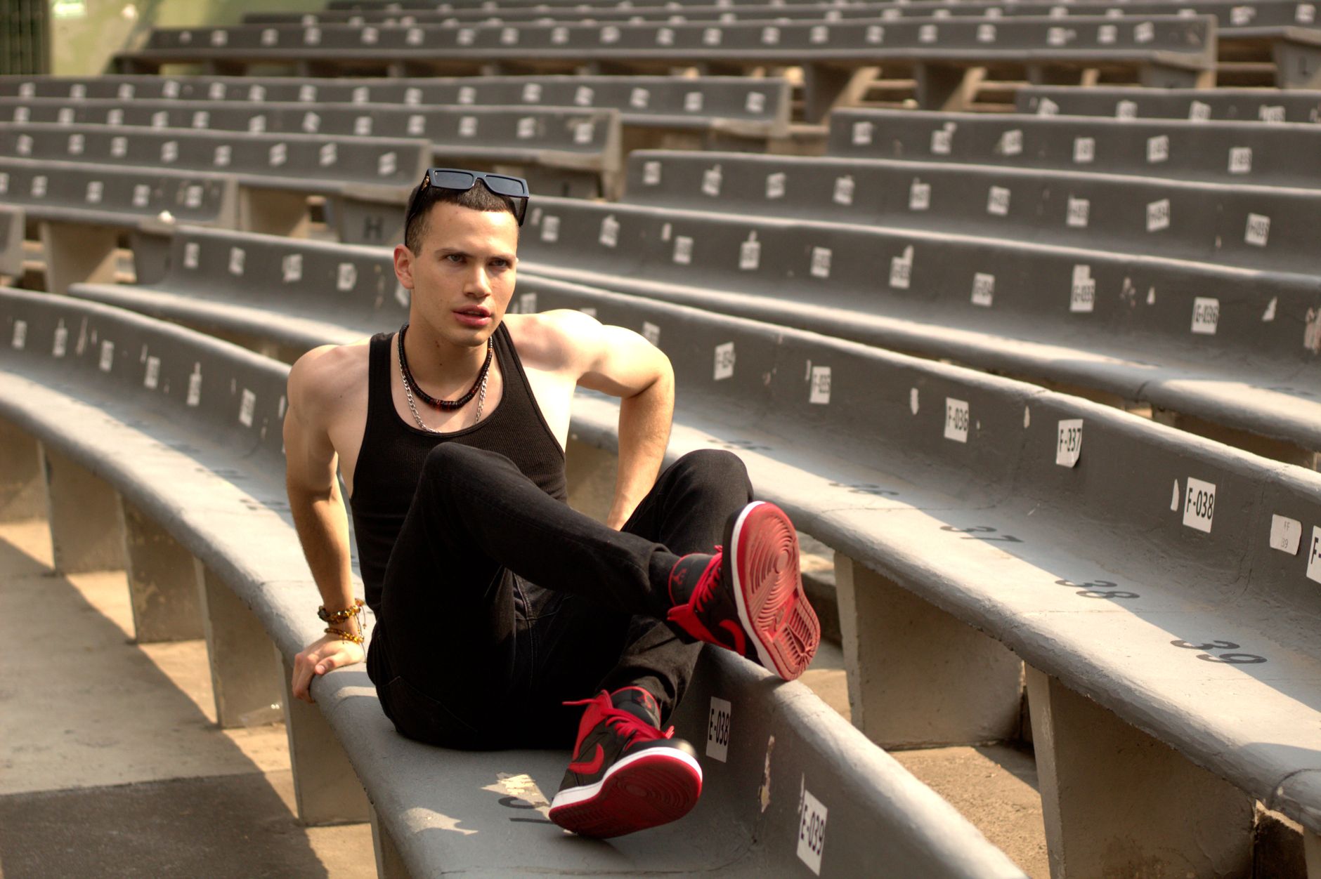 A stylish man relaxes on empty concrete bleachers, enjoying a sunny day.