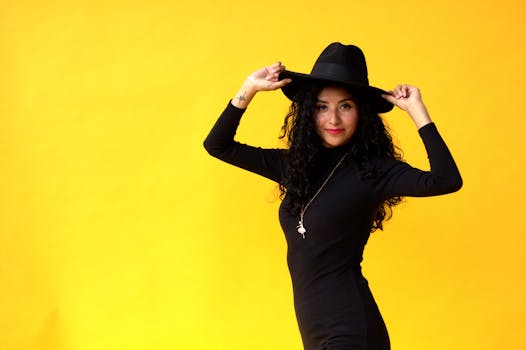 Stylish woman in black posing against a vibrant yellow backdrop, showcasing fashion elegance.
