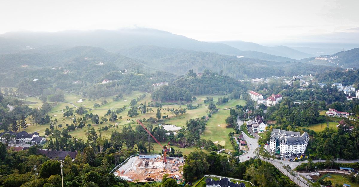 Scenic aerial shot of a town surrounded by misty mountains, forests, and construction site.