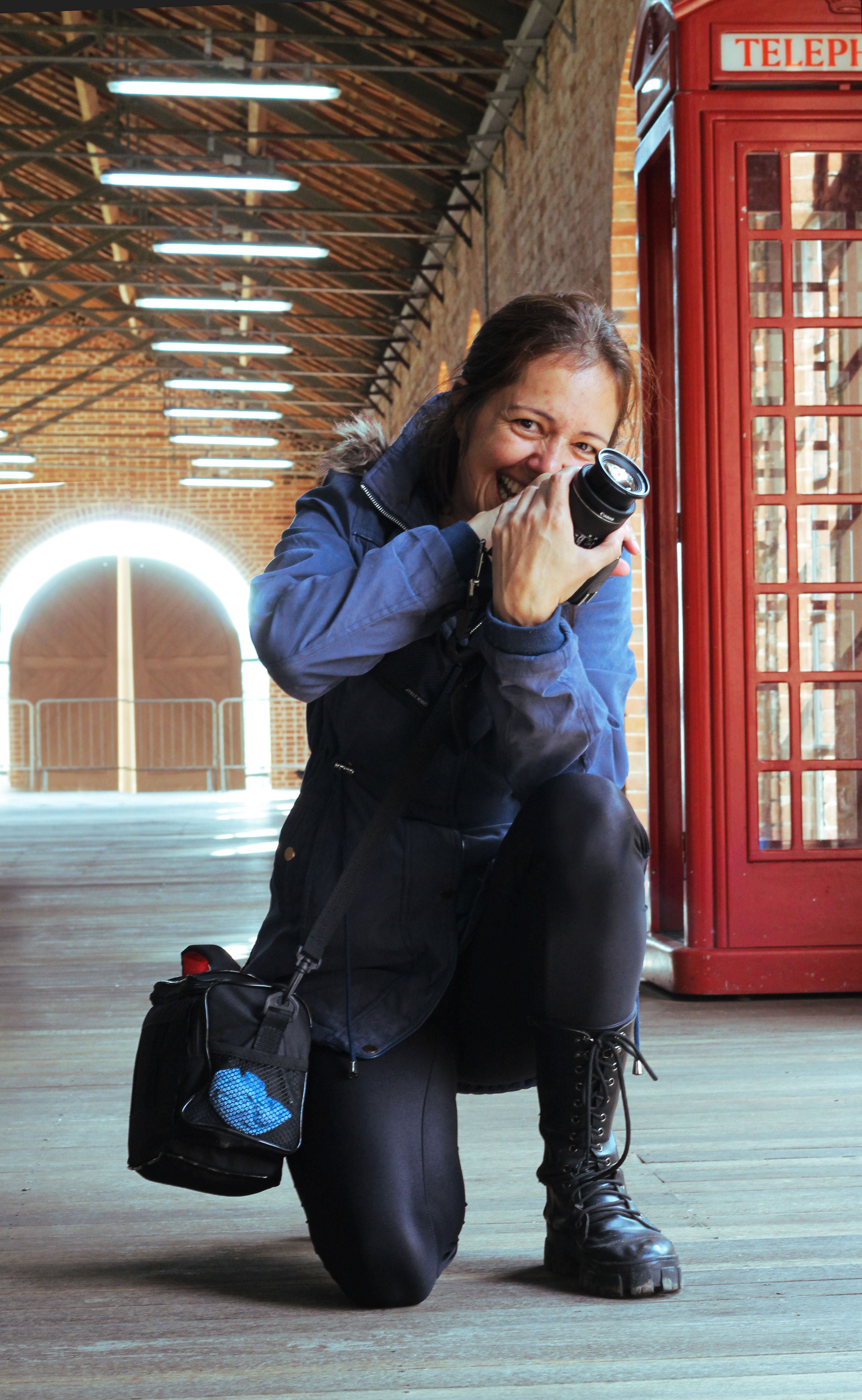 A woman kneels joyfully, capturing a photograph beside a classic red telephone booth.