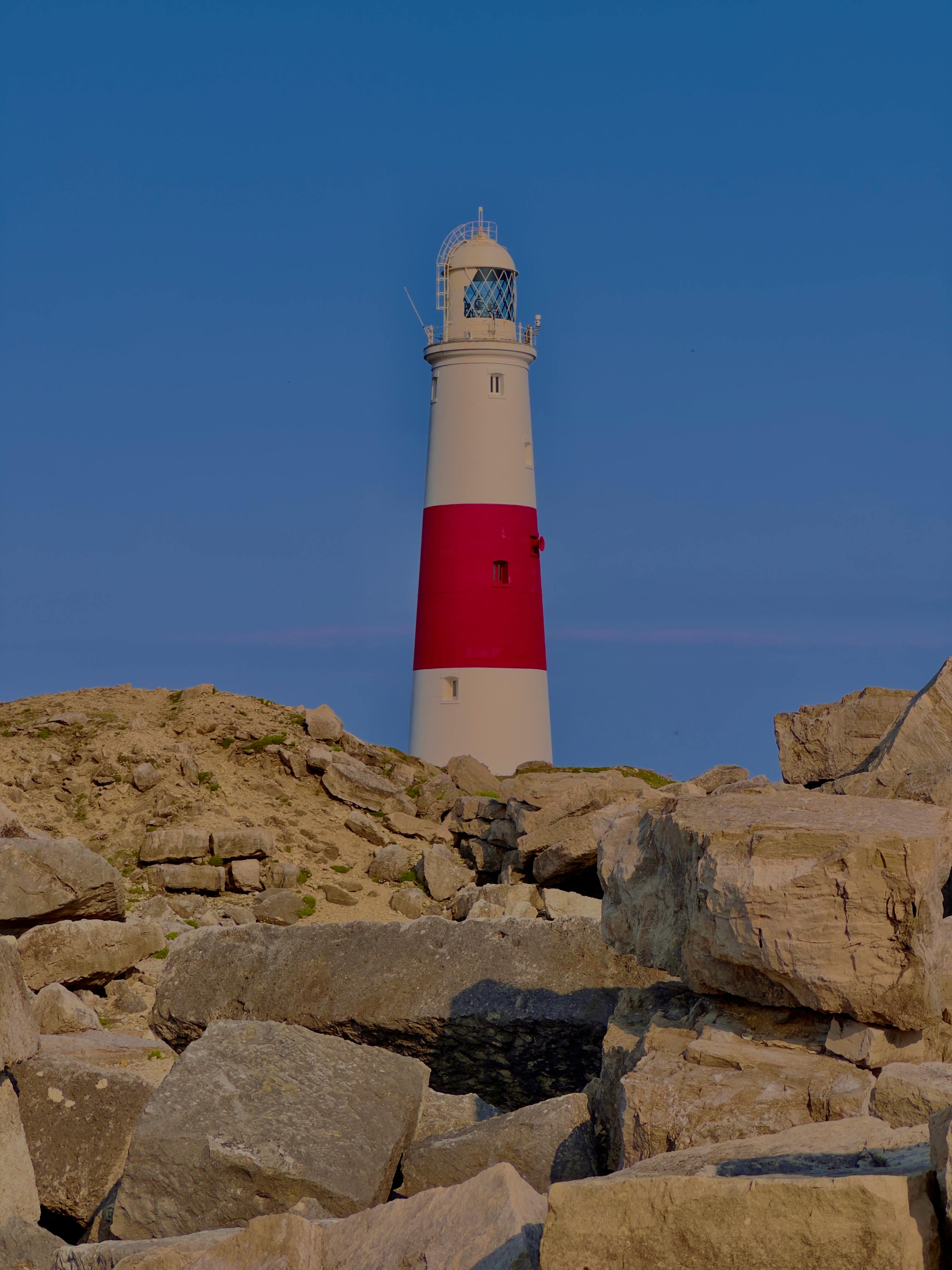 Scenic view of a lighthouse on Portland Bill with rocky foreground during sunset.