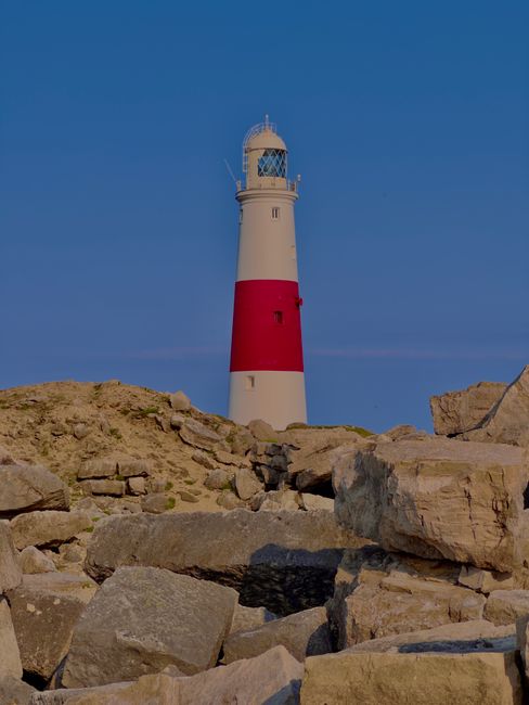 Scenic view of a lighthouse on Portland Bill with rocky foreground during sunset.