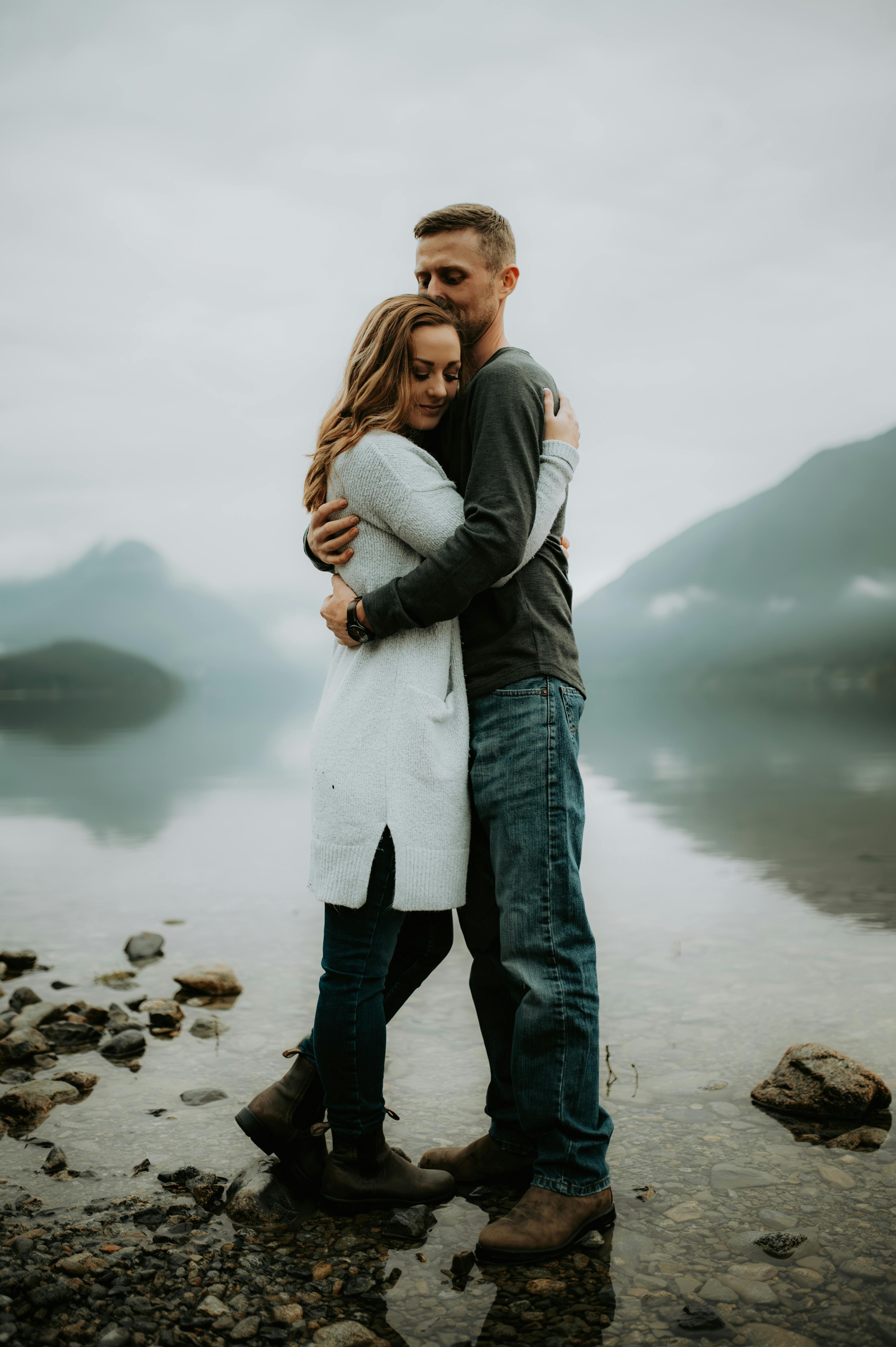 Couple embracing on a tranquil misty mountain riverbank, showcasing nature's serenity.