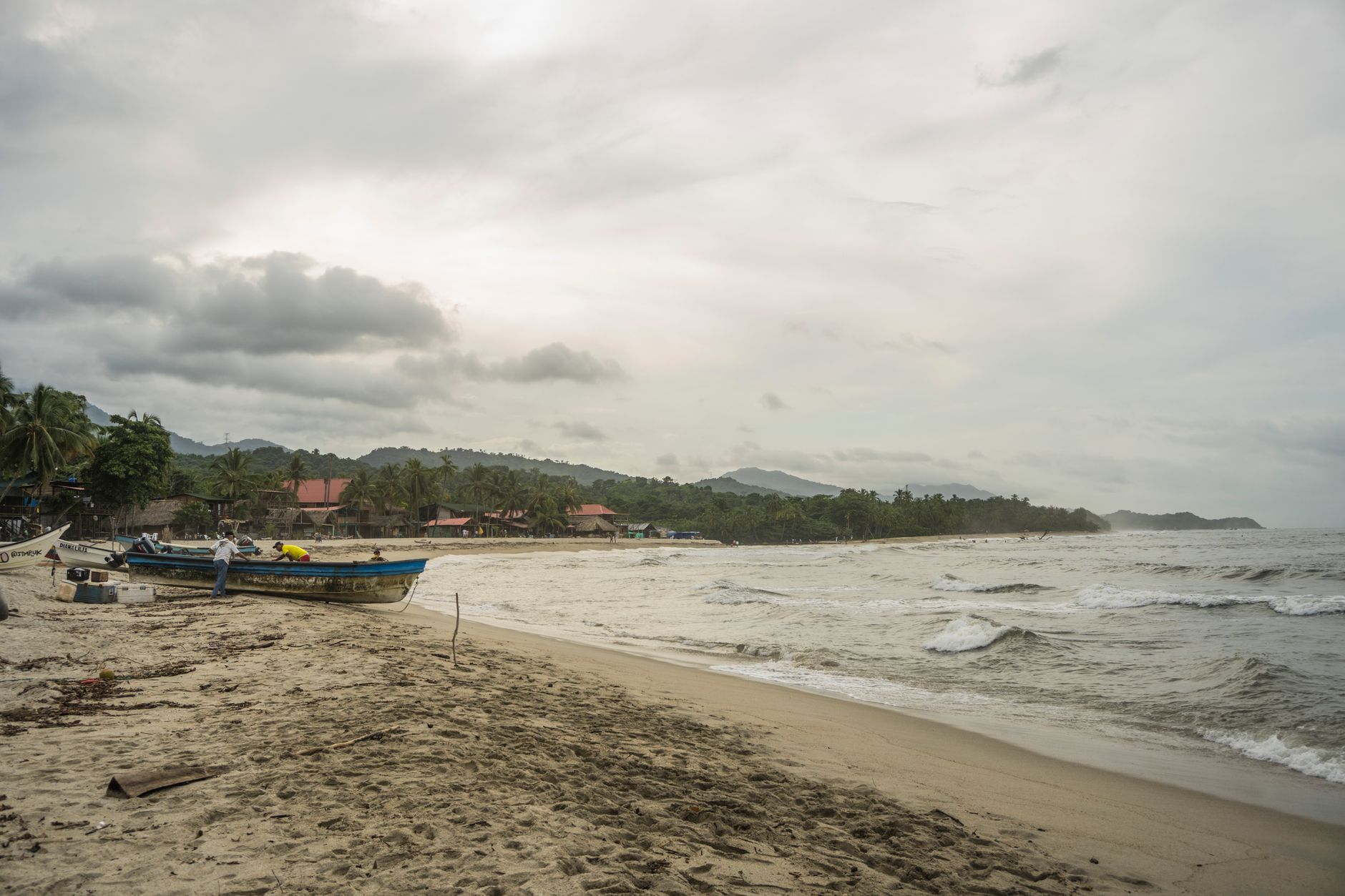 Tranquil beach scene in Palomino, Colombia with boats and palm trees under a cloudy sky.