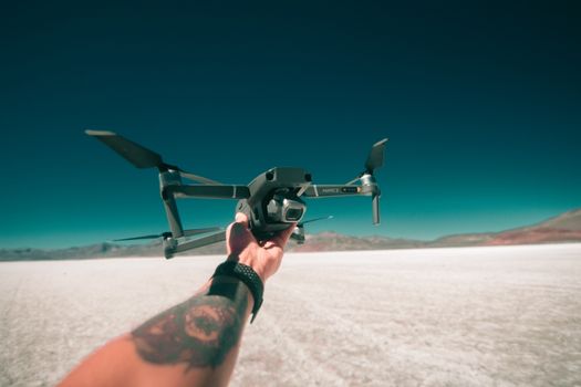 A tattooed arm holds a drone against the arid backdrop of Lima, Peru's stark landscape.