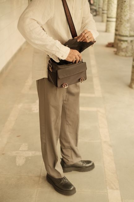Man standing on pavement in New Delhi adjusting a shoulder bag.