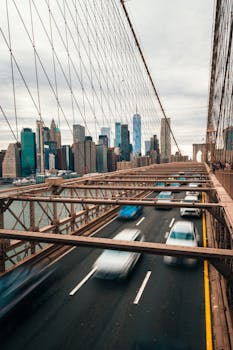 Long exposure of cars on Brooklyn Bridge with Manhattan skyline in view.