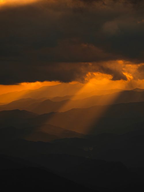 Free Sunlight beams through dark clouds over mountains creating a dramatic and serene atmosphere. Stock Photo