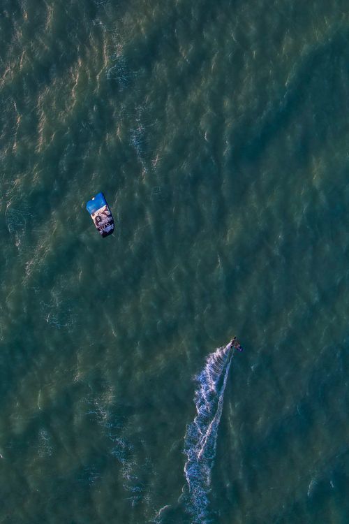 Free Drone shot capturing a kitesurfer navigating the ocean waves, perfect for summer vacation vibes. Stock Photo