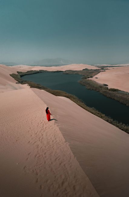Aerial view of a serene oasis in the Pisco desert with a woman in red, under a clear sky in Peru.