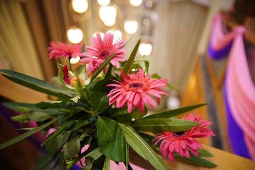 A close-up of vibrant pink gerbera daisies beautifully arranged with green leaves, highlighting the elegant floral decor.