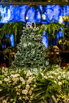 A beautiful 60th birthday celebration cake adorned with lush greenery and white flowers in an indoor setting.
