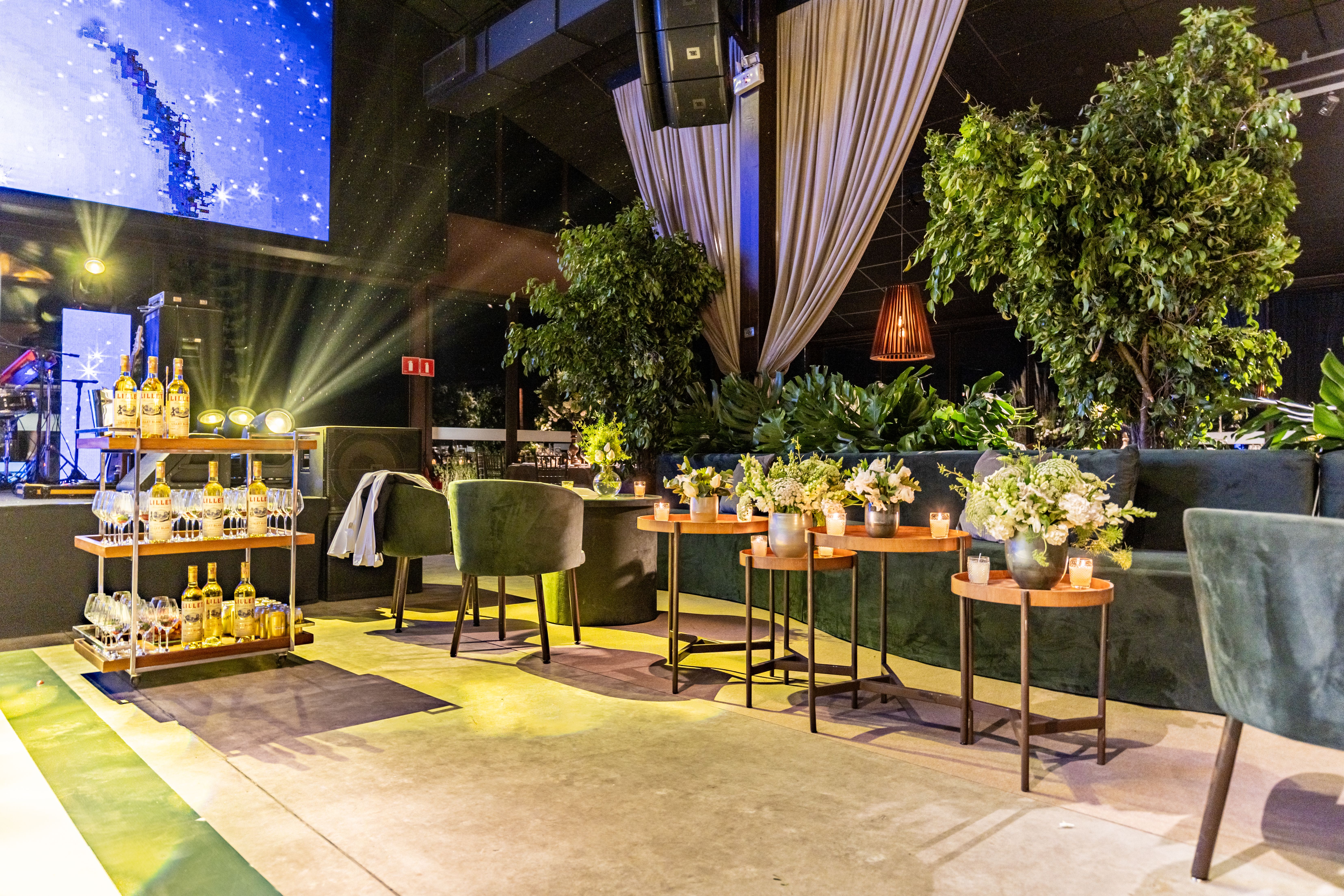 Sophisticated indoor event venue featuring lush plants, bar cart, and cozy seating arrangements.