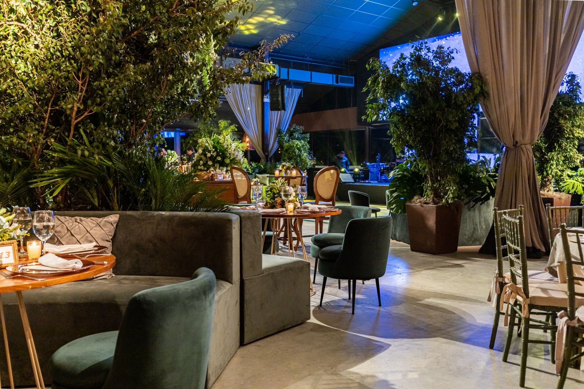 Elegant indoor event venue with greenery, tables, and modern decor, creating a warm ambiance.
