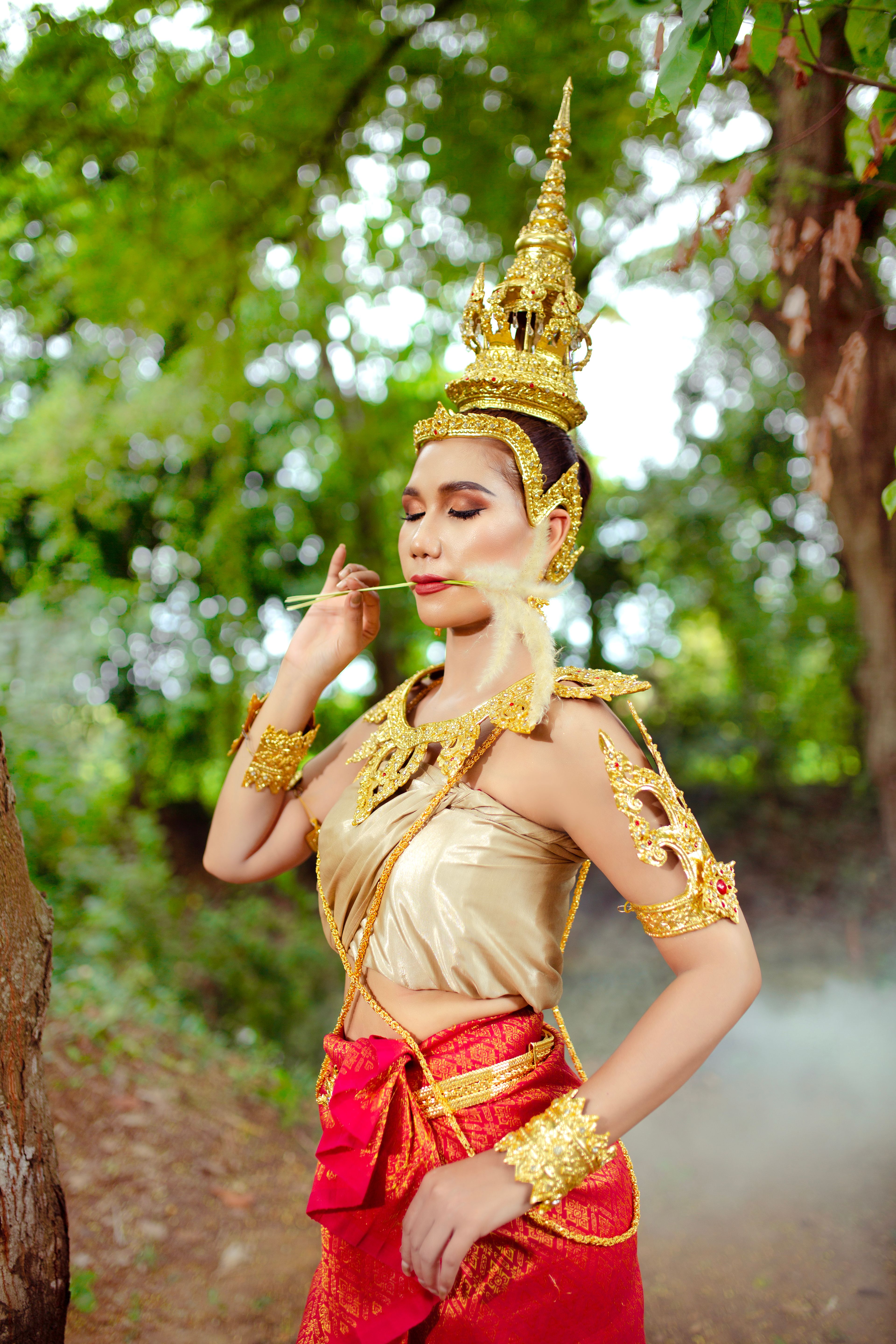 A woman in traditional Cambodian attire posing outdoors with a golden headdress and jewelry.