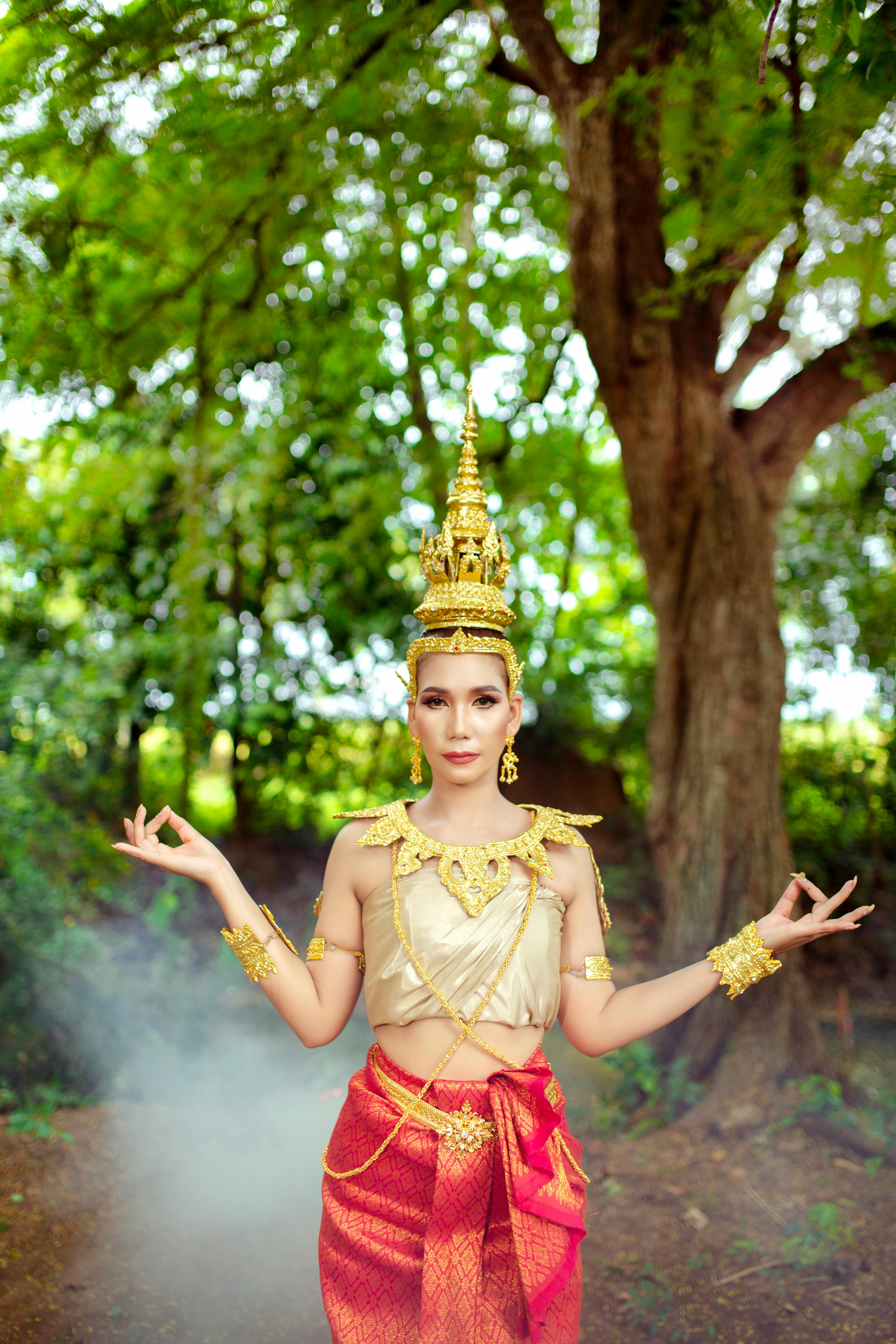 A woman in traditional Cambodian attire poses gracefully in a forest setting.