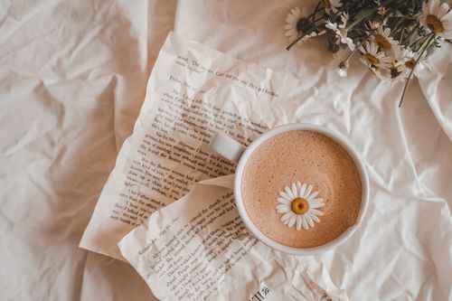 Free A cup of coffee with a daisy on a bed of book pages and flowers, creating a cozy, artistic scene. Stock Photo