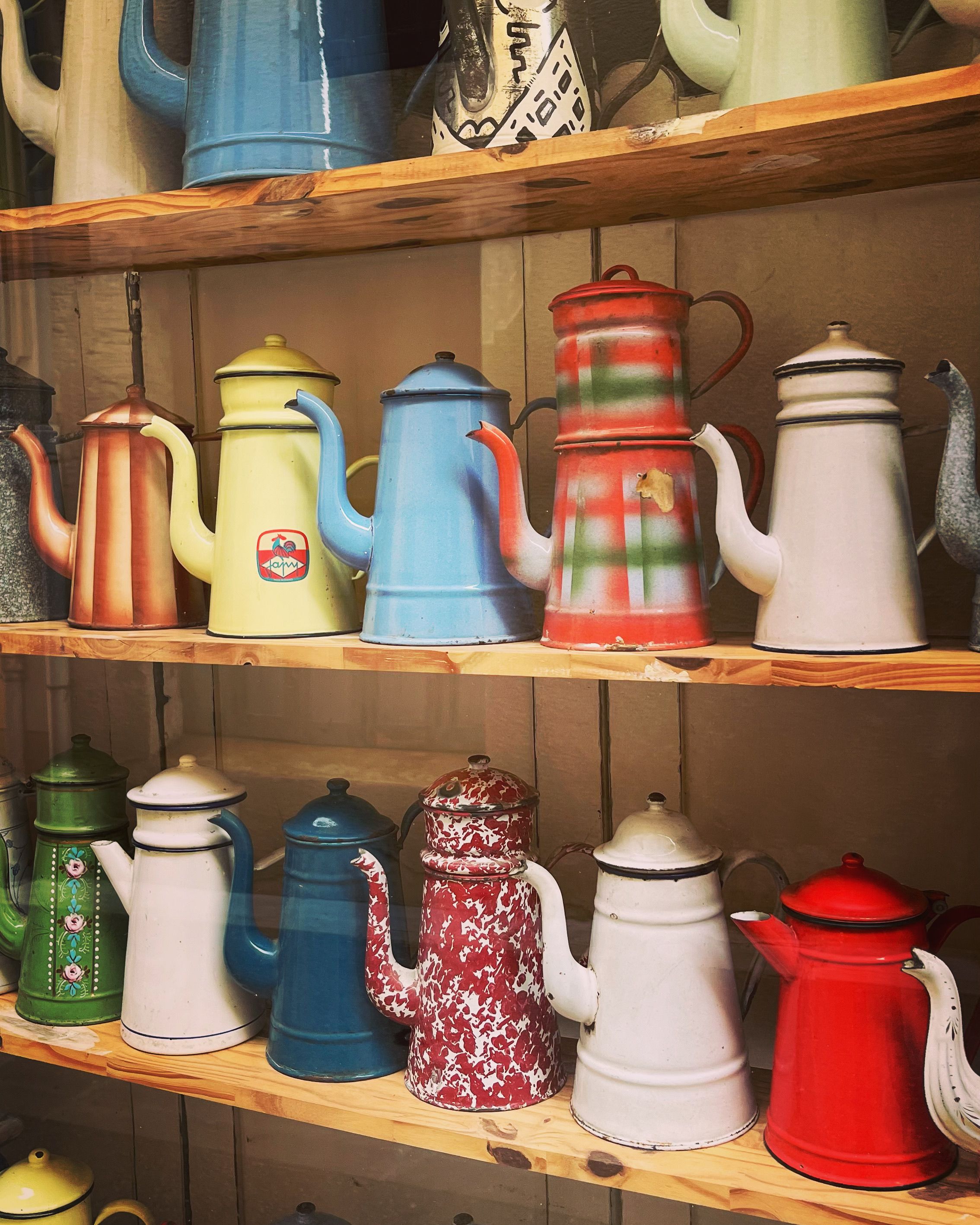 A vibrant display of vintage enamel coffee pots on wooden shelves, showcasing diverse colors and styles.