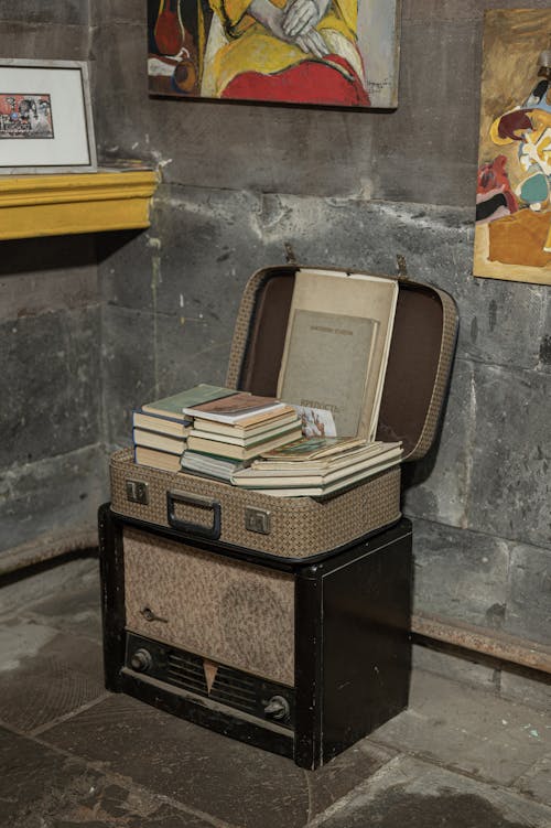 View of a Suitcase Full of Books Standing on a Vintage Radio by a Wall with Art 