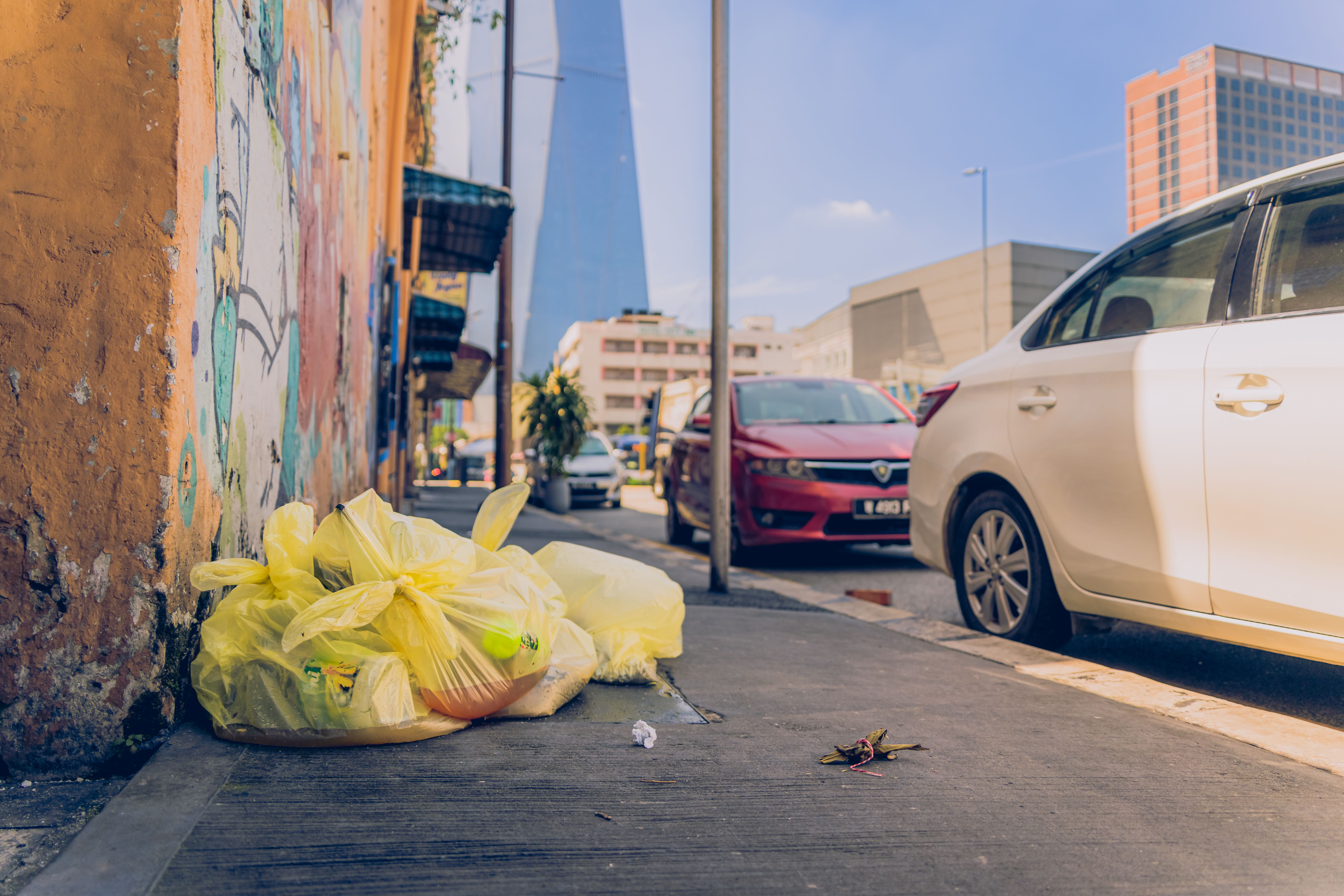 Yellow bags of trash on a Kuala Lumpur sidewalk with city backdrop.