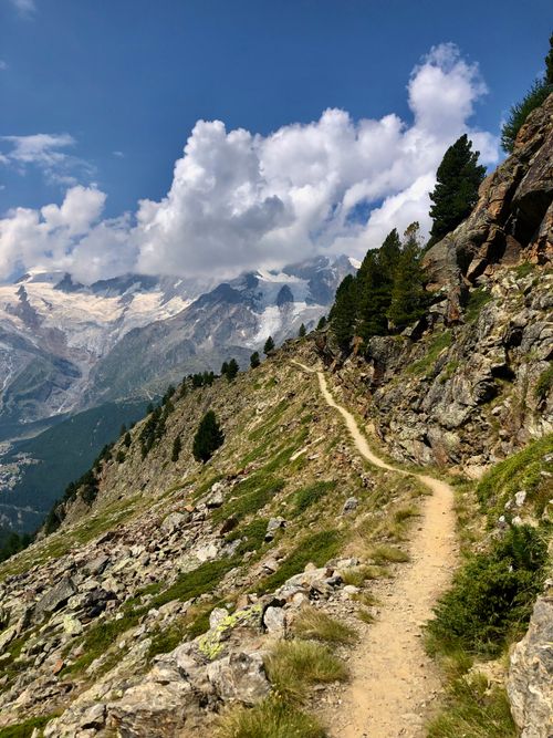 Free A winding mountain path surrounded by lush greenery and towering peaks under a clear sky. Stock Photo