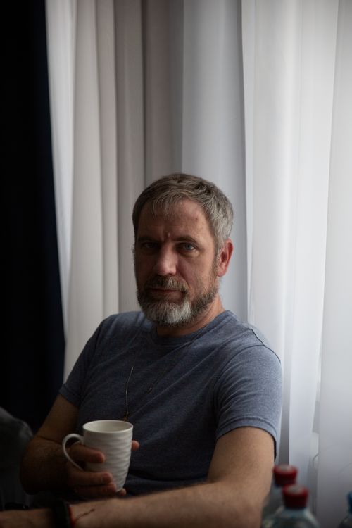 Free Middle-aged man with a beard holding a mug, relaxing indoors by a window in soft light. Stock Photo